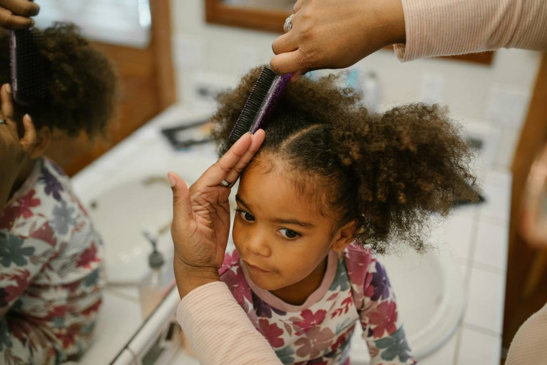 child getting her hair combed by an adult in the bathroom