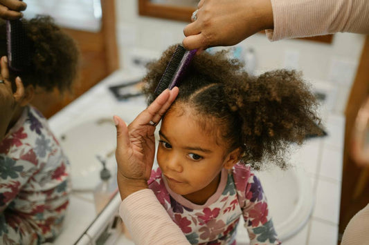child getting her hair combed by an adult in the bathroom